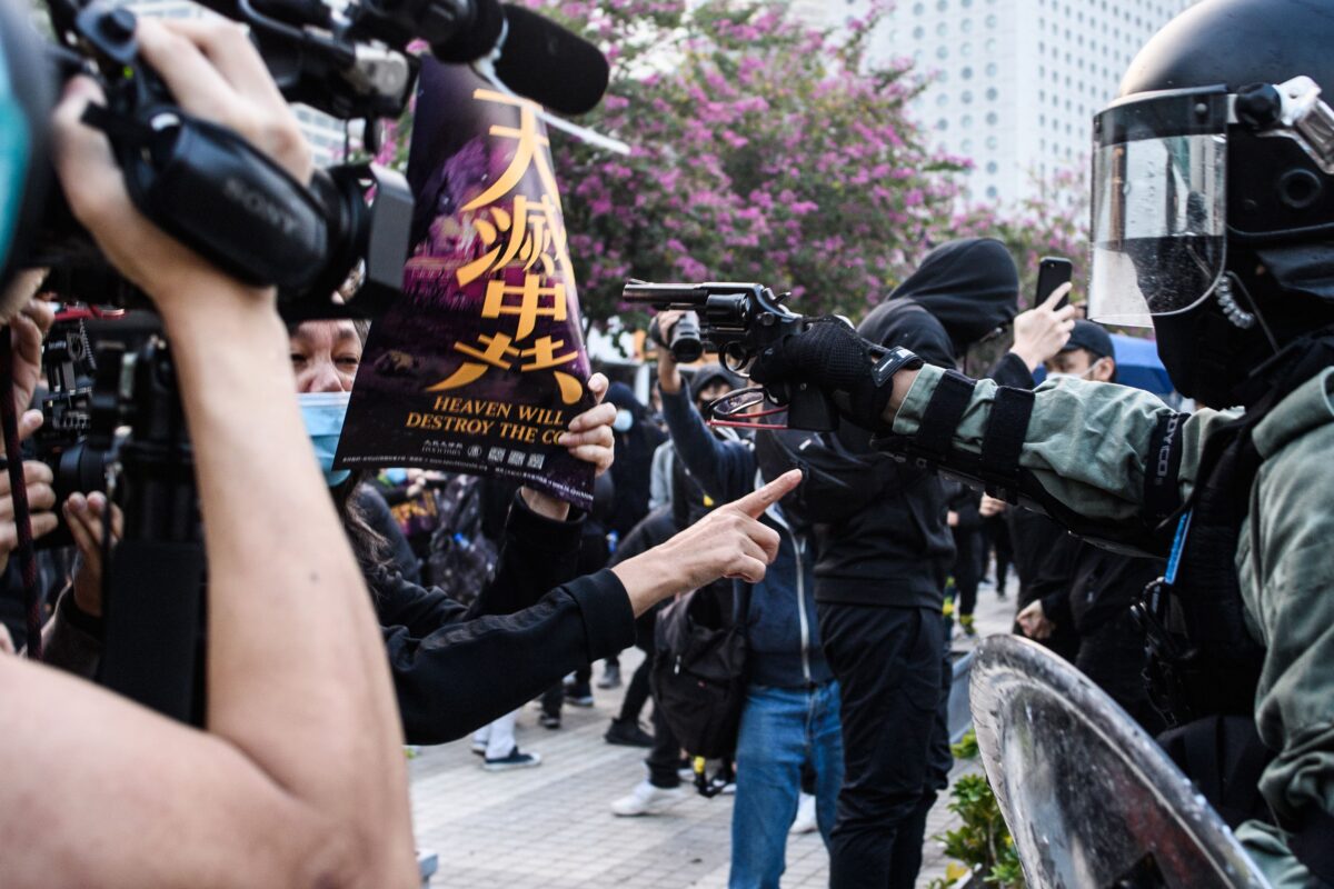 Policejní důstojník míří pistolí na protestující během shromáždění v Hongkongu 22. prosince 2019, zatímco se jej kolegové evidentně pokoušejí strhnout, aby nestřílel. (Anthony Wallace / AFP / Getty Images)