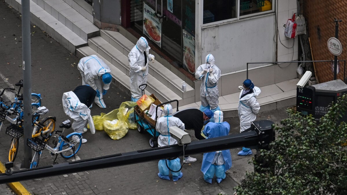 Pracovníci si svlékají ochranné pomůcky u vchodu do čtvrti během druhé fáze pandemického lockdownu ve čtvrti Jing'an v Šanghaji, 5. dubna 2022. (Hector Retamal / AFP via Getty Images)